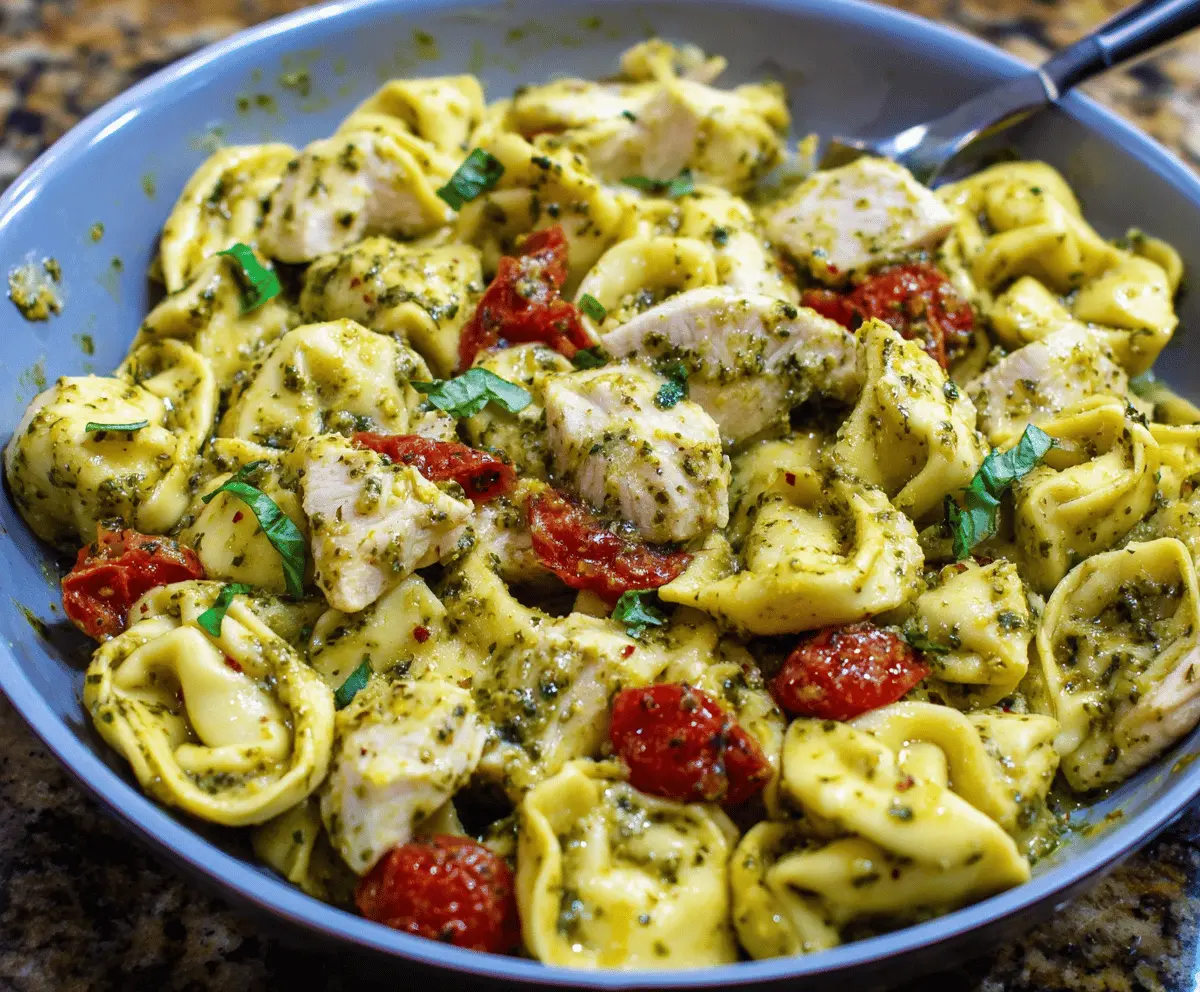 Creamy pesto chicken tortellini dish garnished with fresh basil and grated Parmesan cheese on a white plate