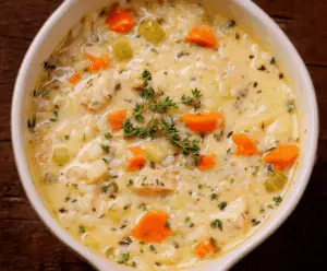 Creamy chicken and rice soup in a bowl with fresh herbs and a spoon, showcasing a comforting, hearty dish with tender chicken, rice, and creamy broth.