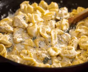 Creamy Garlic Parmesan Chicken Tortellini served with fresh herbs and grated cheese on a white plate, highlighting a delicious pasta dish with tender chicken and flavorful garlic and Parmesan sauce.