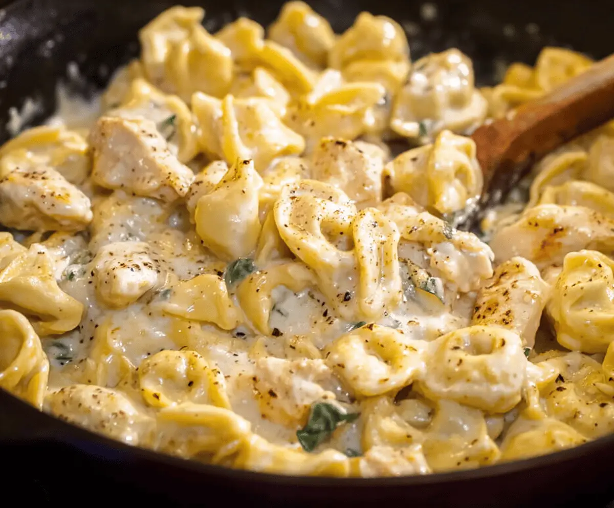 Creamy Garlic Parmesan Chicken Tortellini served with fresh herbs and grated cheese on a white plate, highlighting a delicious pasta dish with tender chicken and flavorful garlic and Parmesan sauce.