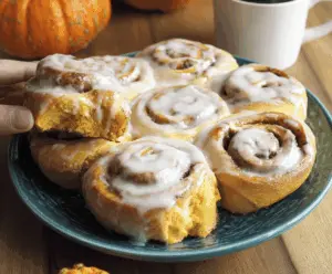 Delicious pumpkin cinnamon rolls topped with icing on a plate, perfect for fall desserts and breakfast treats.