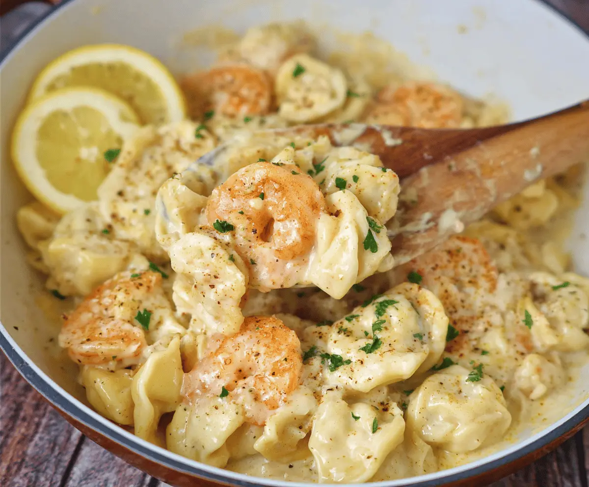 Delicious shrimp tortellini pasta topped with lemon garlic cream sauce and fresh herbs, served on a white plate.