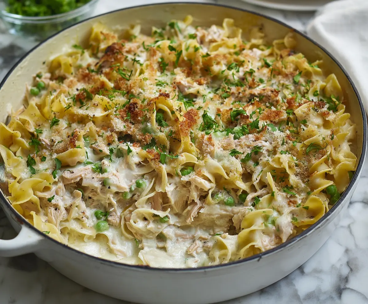 Delicious creamy tuna noodle casserole garnished with fresh herbs, served in a white baking dish.